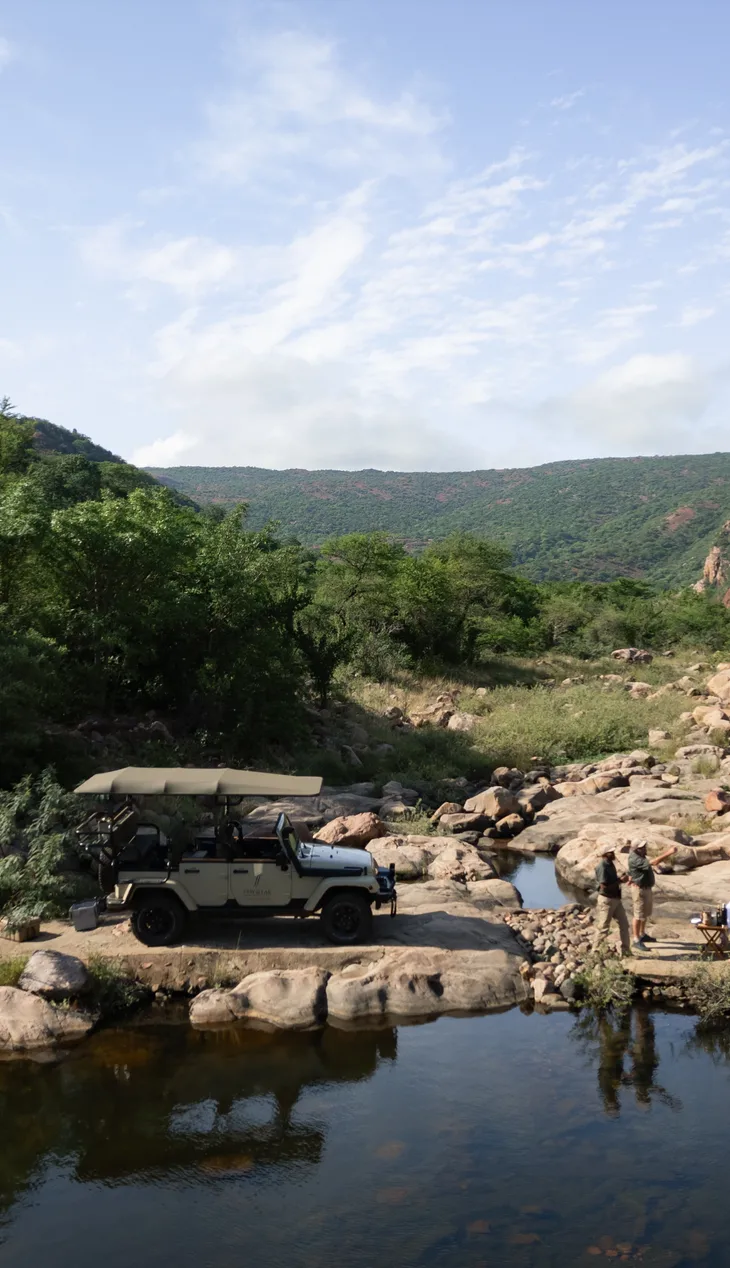 Guided game-drive vehicle beside a rocky river