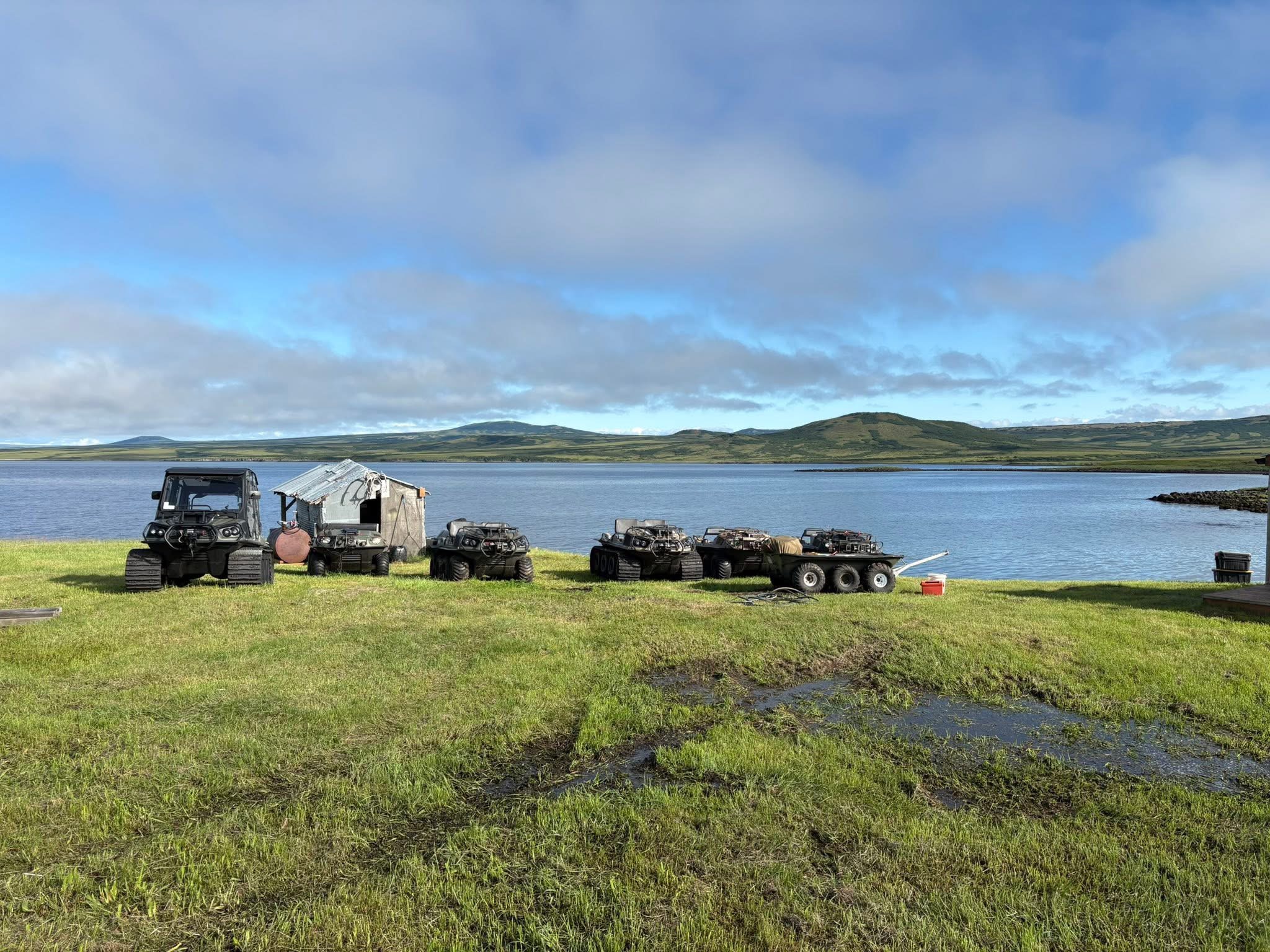 Tracked and all-terrain vehicles lined up beside the lake at camp