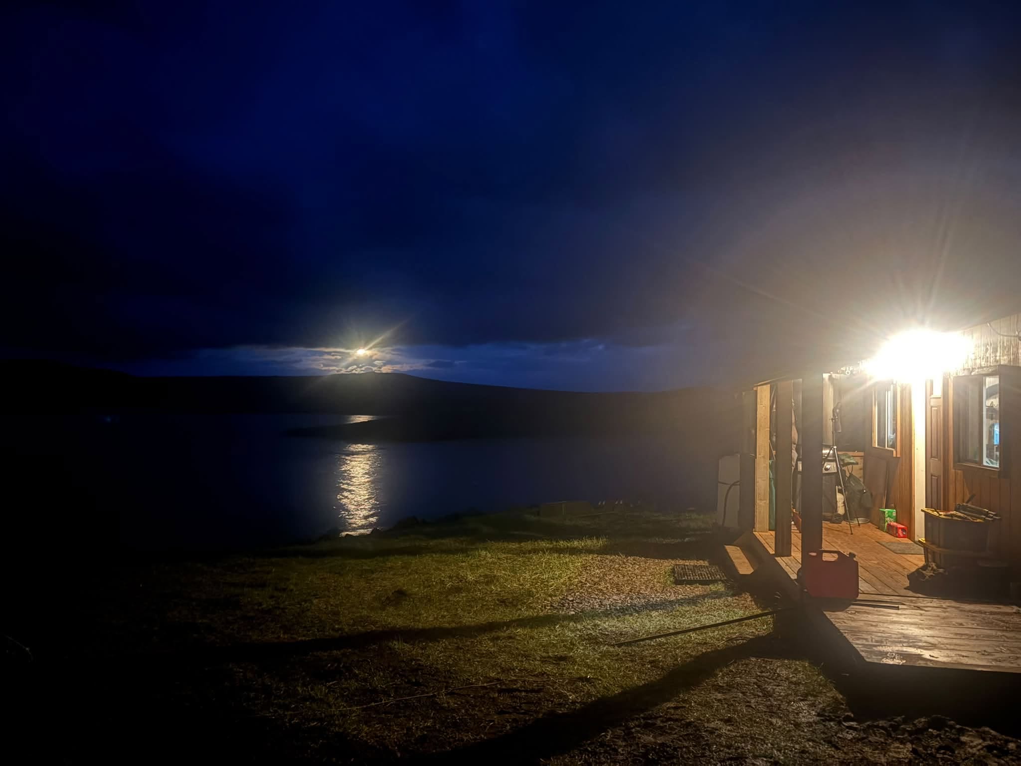 Moonlight reflecting on the lake beside the lit cabin porch