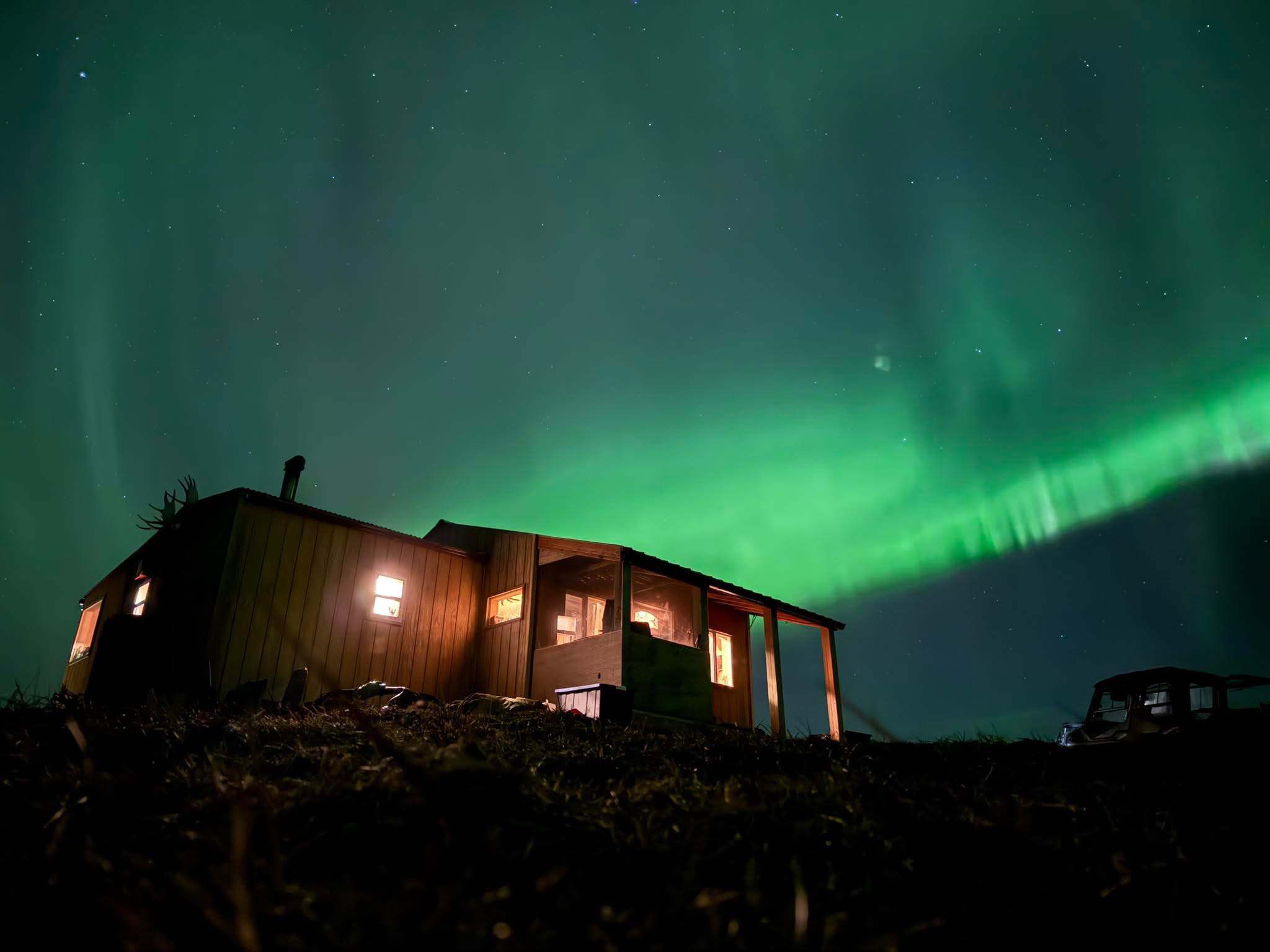 Northern lights above the illuminated Alaska camp cabin